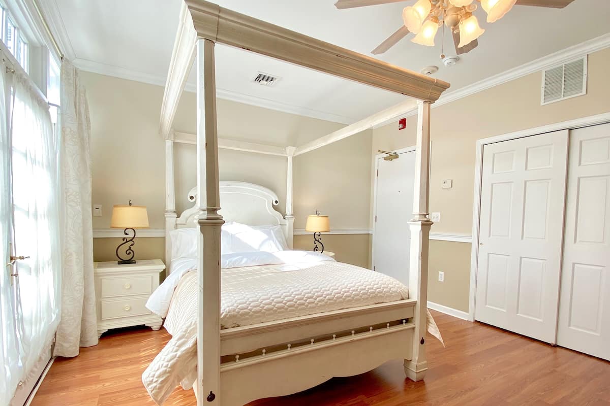 A four-poster bed with a canopy, a nightstand with a lamp, a dresser, and a double door.
