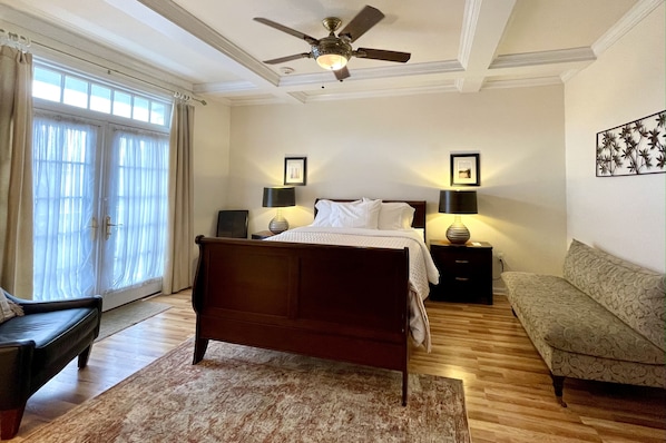 A bedroom with a bed, bedside lamps, a ceiling fan, a sofa, and a window with curtains.