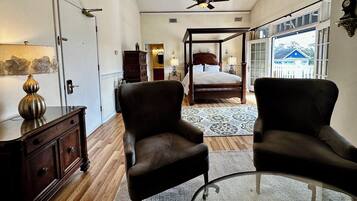 A bedroom with a four-poster bed, a sitting area with two armchairs, a wooden dresser, and a lamp.