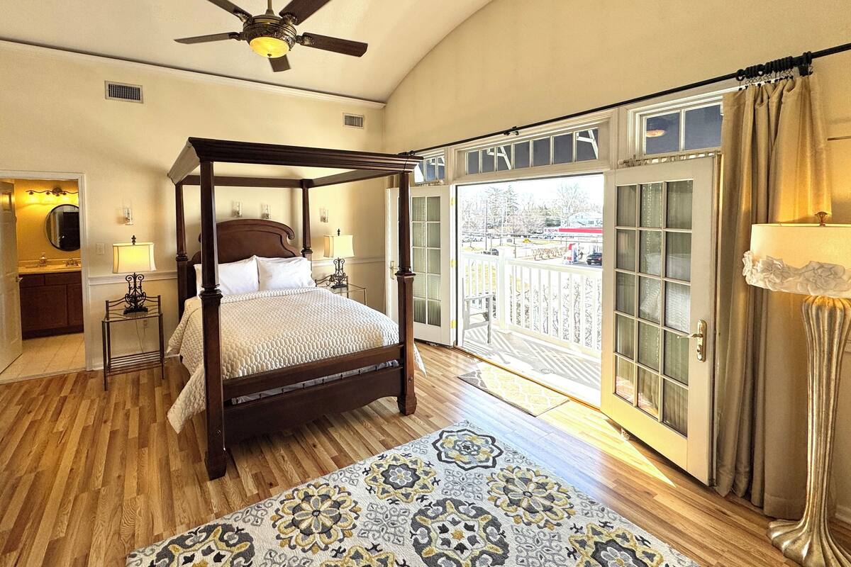A four-poster bed with a wooden frame, a patterned rug, and a view of a parking lot through a glass door.