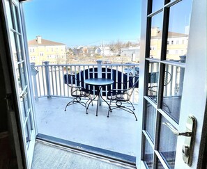 A balcony with a round table and four chairs, overlooking a residential area with houses and a clear sky.