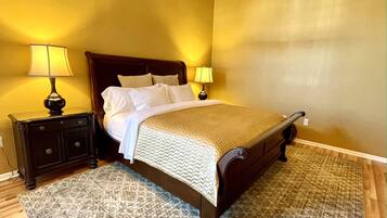 A neatly made bed with a wooden headboard, two bedside tables with lamps, and a patterned rug on a wooden floor.