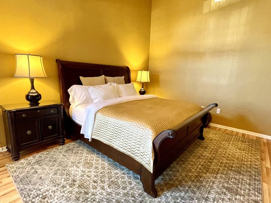 A neatly made bed with a wooden headboard, two bedside tables with lamps, and a patterned rug on a wooden floor.