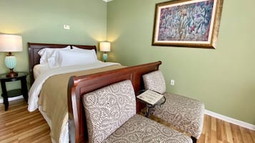 Ein ordentlich eingerichtetes Hotelzimmer mit einem Bett, zwei gemusterten Stühlen, einem kleinen Tisch und einer gerahmten Blumenleiste an der Wand.