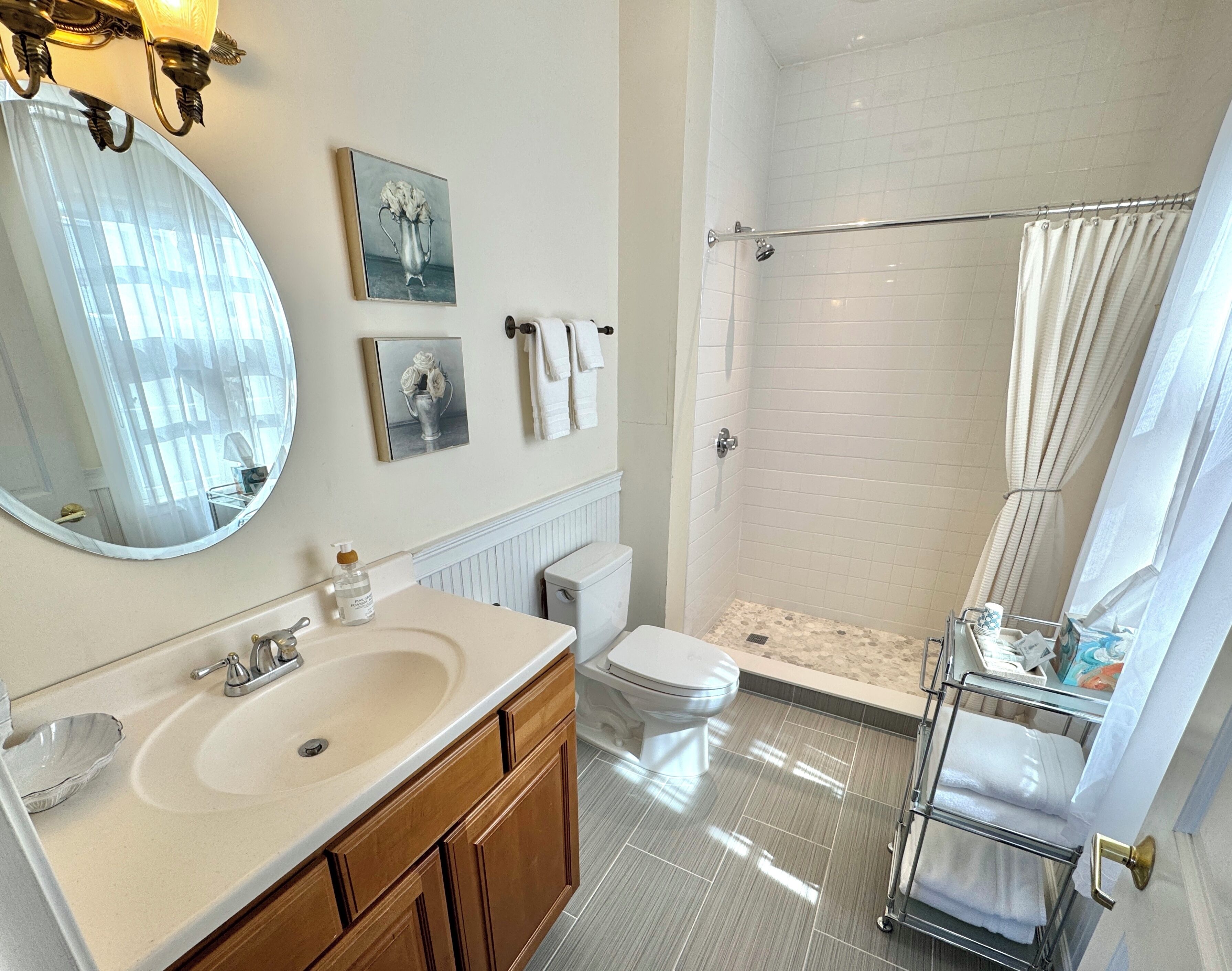 Un bagno moderno con un ampio specchio, un lavandino con dispenser di sapone, un water, una doccia con porta in vetro e un portascopevoli.