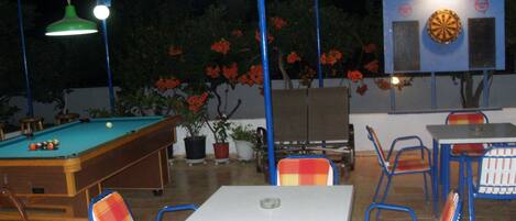 An outdoor pool area with a pool table, chairs, and a dartboard.