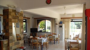A dining area with multiple tables and chairs, a television, and a safe box. - Vera Studios (Rhodes)