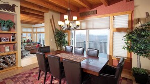A dining area with a wooden table, chairs, and a chandelier. There is a window with blinds, a plant, and a view of the outside. - Solitude Village at Okemo  by Vail Resorts (Ludlow)