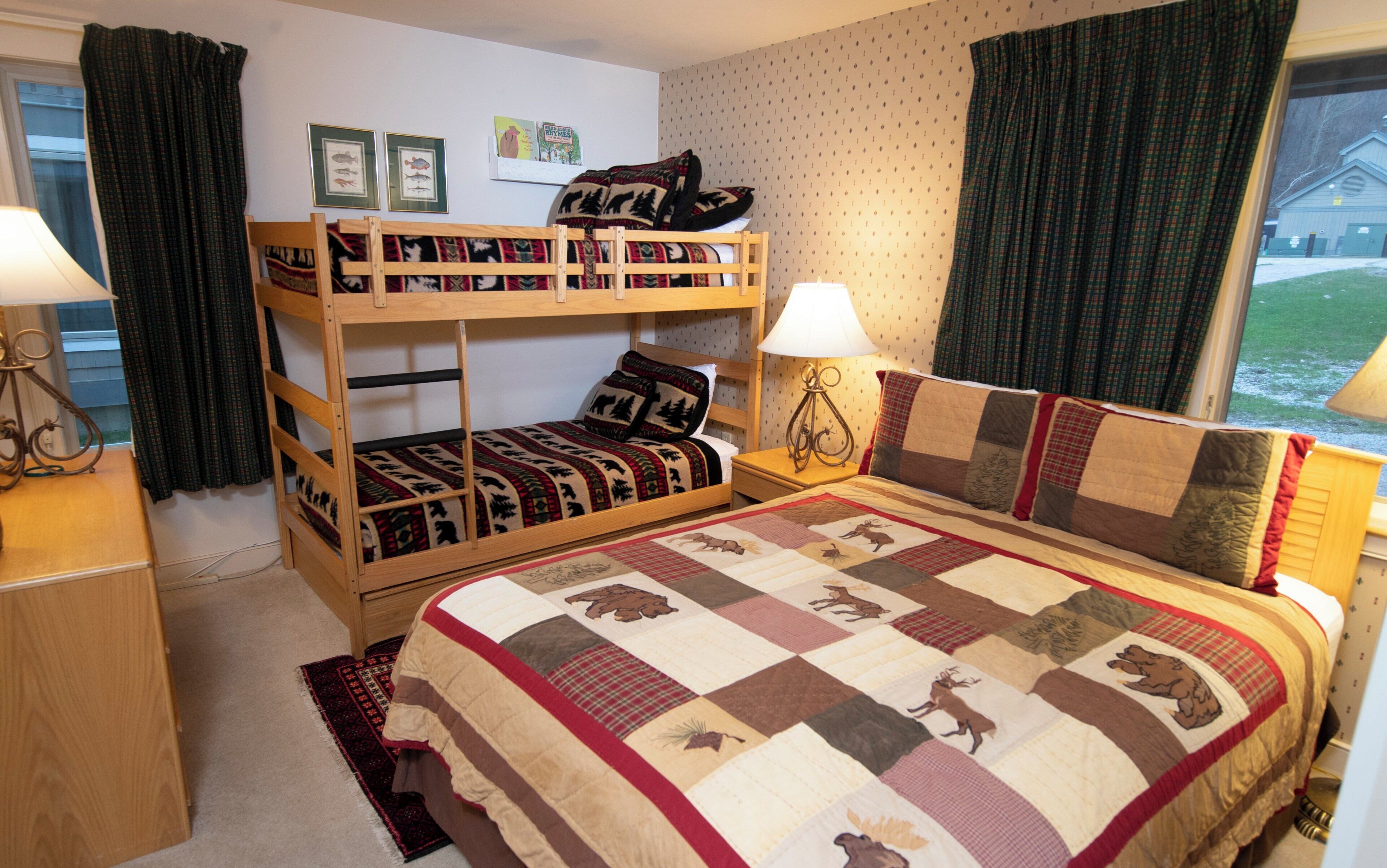 A bunk bed room with a quilted bedspread, a wooden desk, and a lamp.