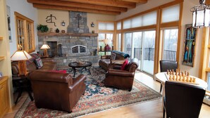 A spacious living room with leather sofas, a stone fireplace, and a large window offering a view. - Solitude Village at Okemo  by Vail Resorts (Ludlow)