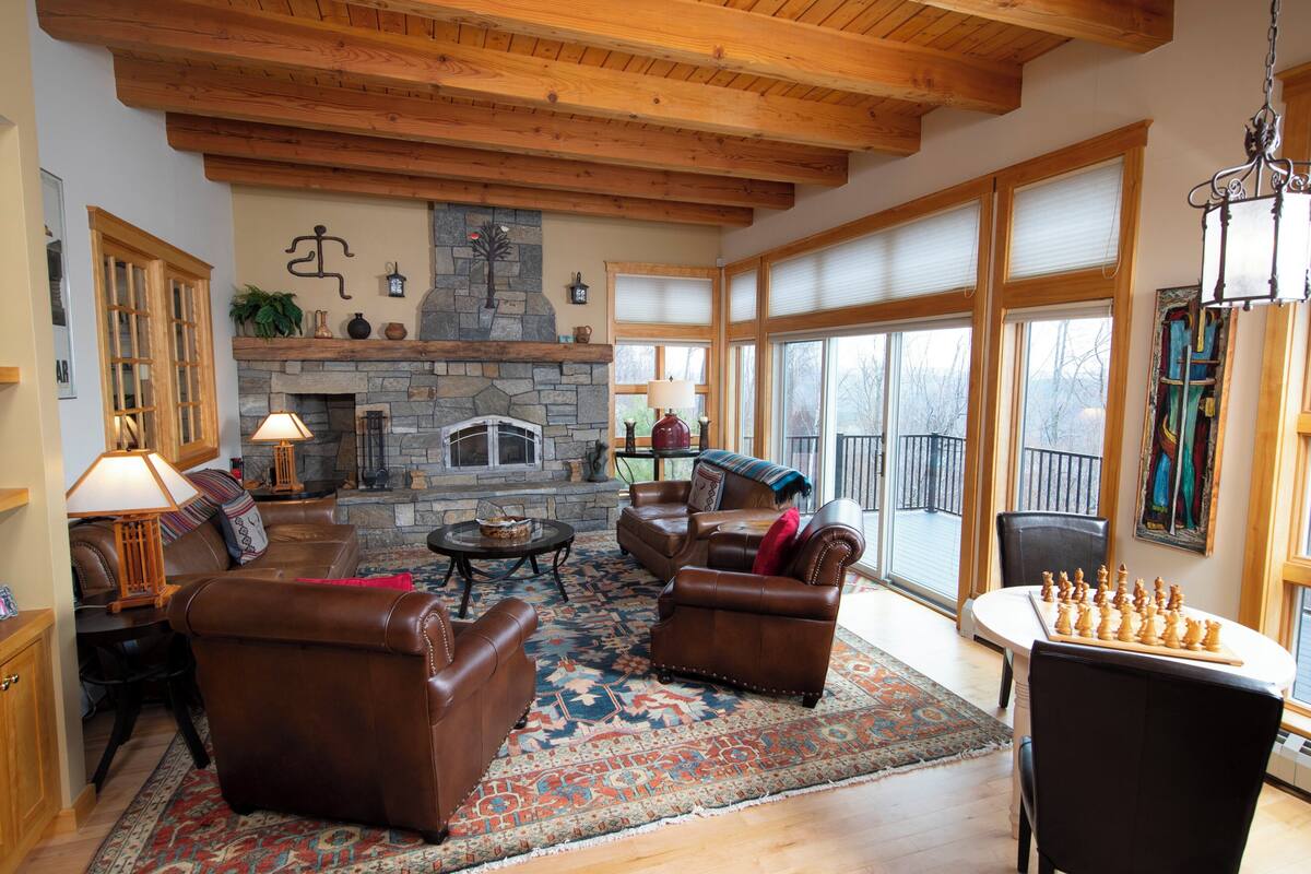 A spacious living room with leather sofas, a stone fireplace, and a large window offering a view.