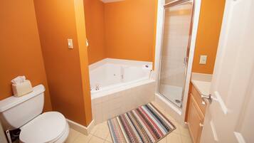 Un baño con una pared naranja, una bañera blanca, un cerramiento de ducha de vidrio y una alfombra estampada.