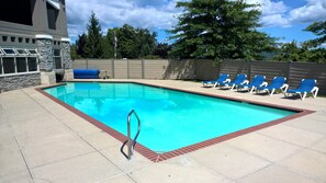A rectangular swimming pool with a red border, surrounded by a concrete deck. There are blue lounge chairs aligned along the pool's edge.