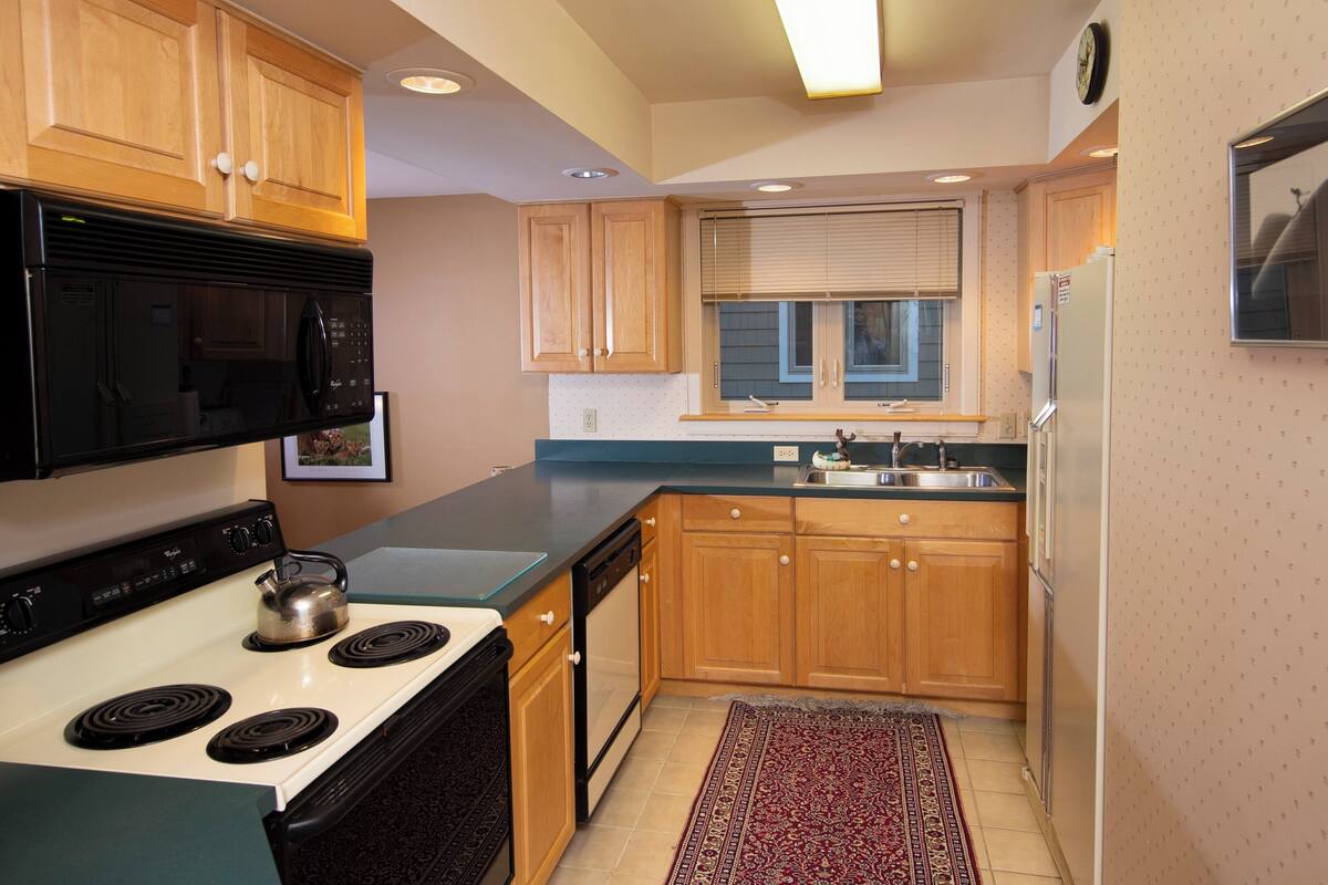 A compact kitchen with wooden cabinets, a black microwave, a stove, and a refrigerator.