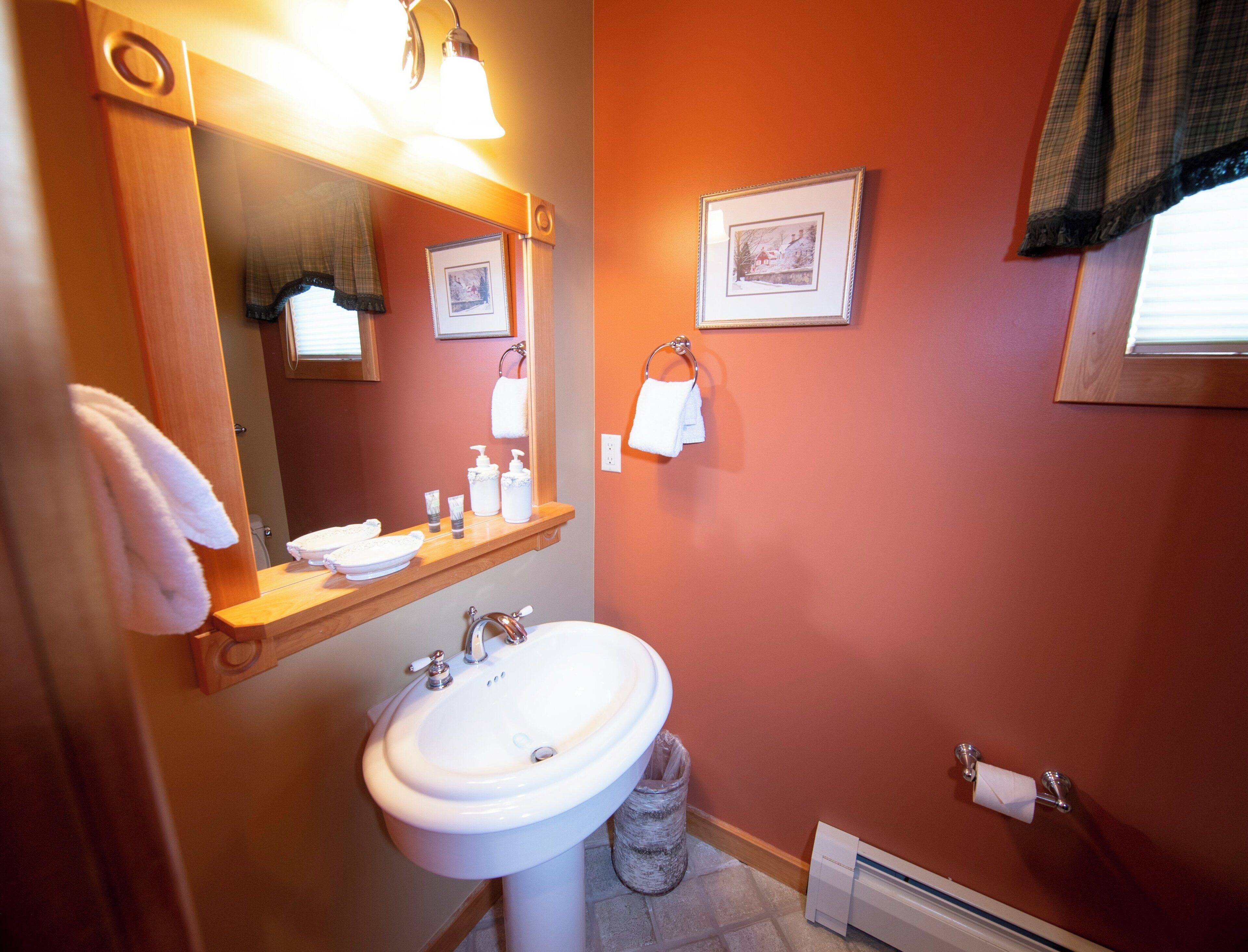 A bathroom with a white sink, a mirror above it, and a wooden shelf with toiletries.