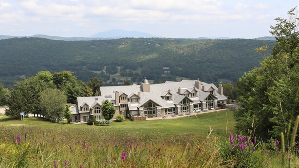 A large, multi-story building with a symmetrical facade, surrounded by a well-maintained lawn and wildflowers. - Solitude Village at Okemo  by Vail Resorts (Ludlow)
