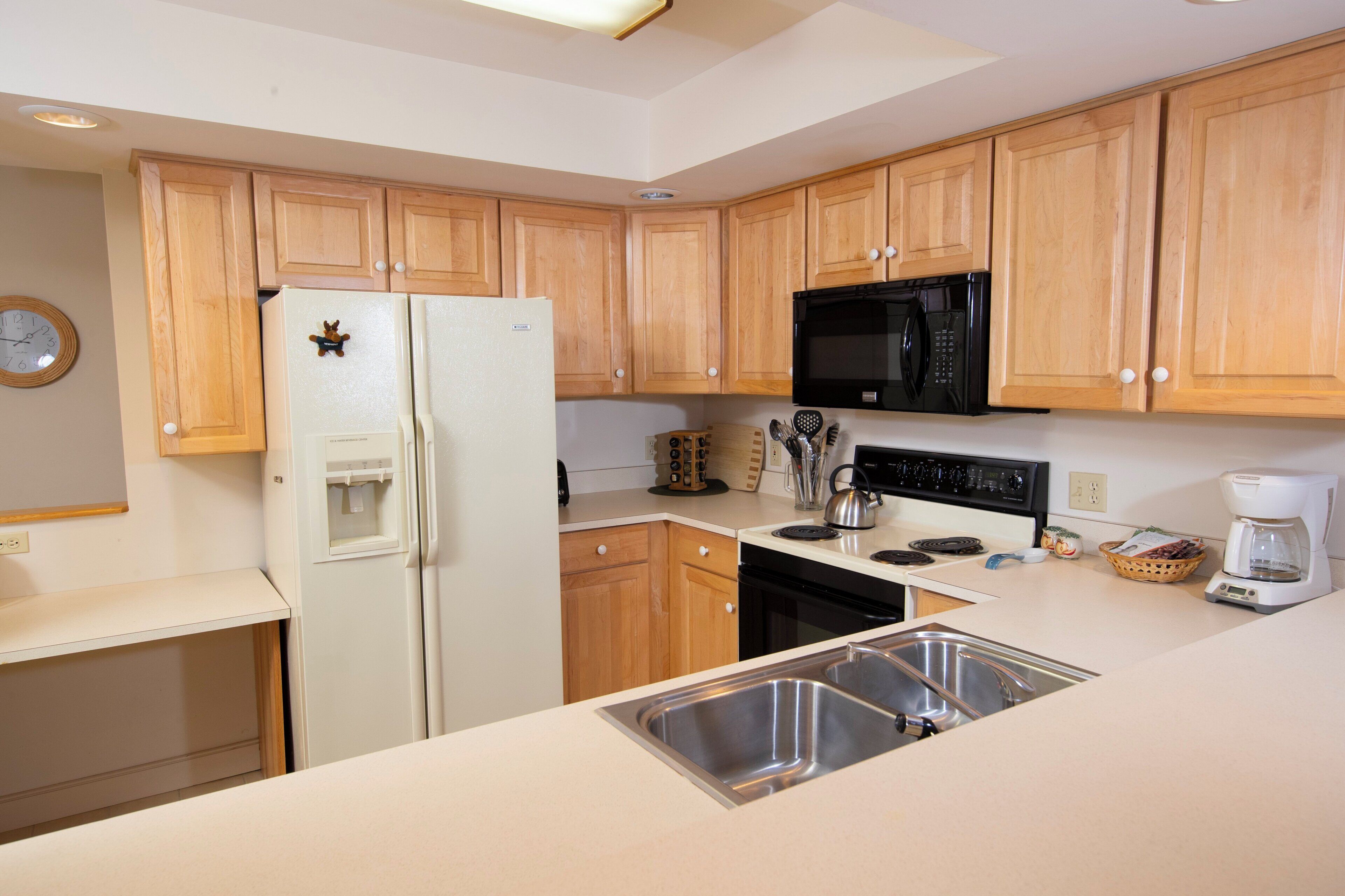 A kitchen with wooden cabinets, a white refrigerator, a black microwave, a sink, and a coffee maker.
