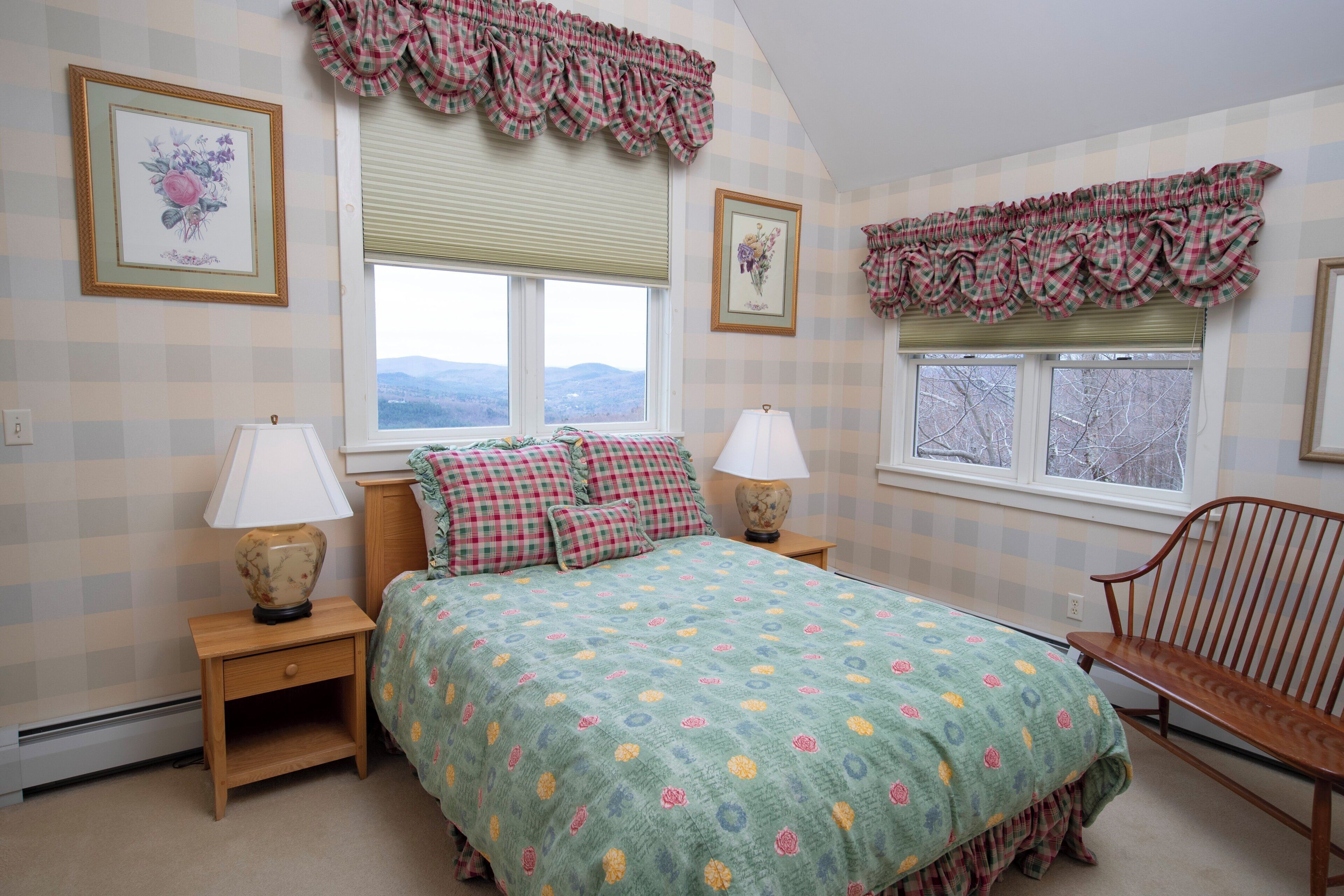 A bedroom with a bed, two nightstands, a chair, and a window with a view of mountains.