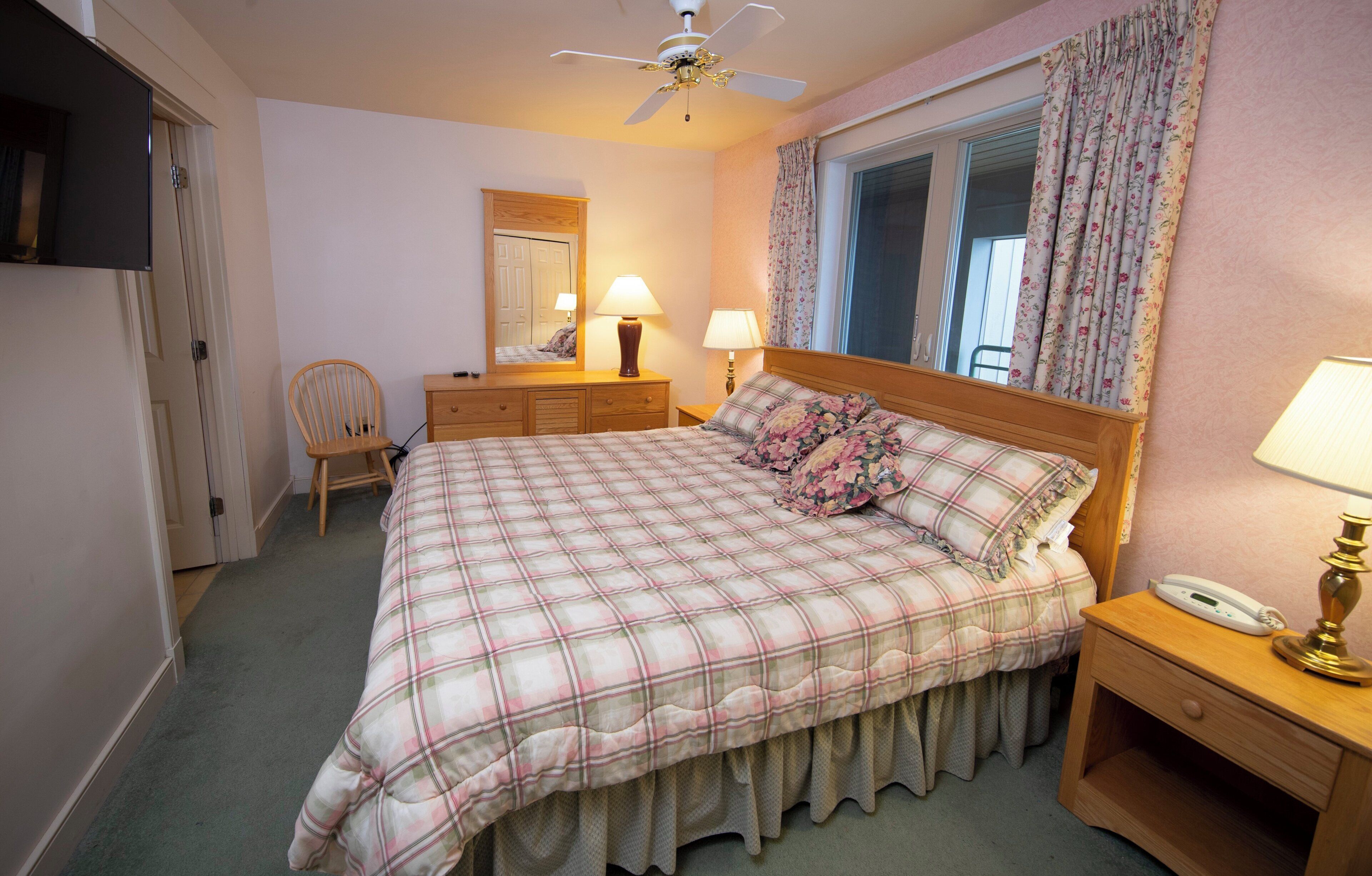 Une chambre à coucher comprenant un lit, une table de chevet, une lampe, une chaise, une commode et un ventilateur de plafond.