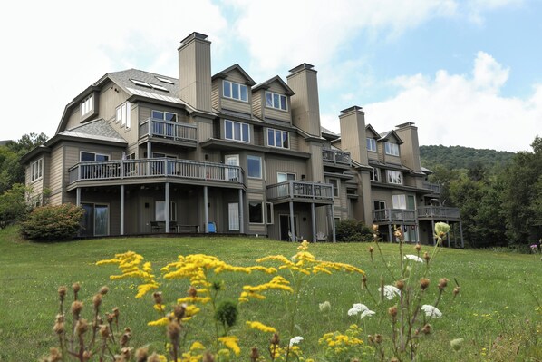 A large, multi-story house with multiple balconies and a spacious front lawn.