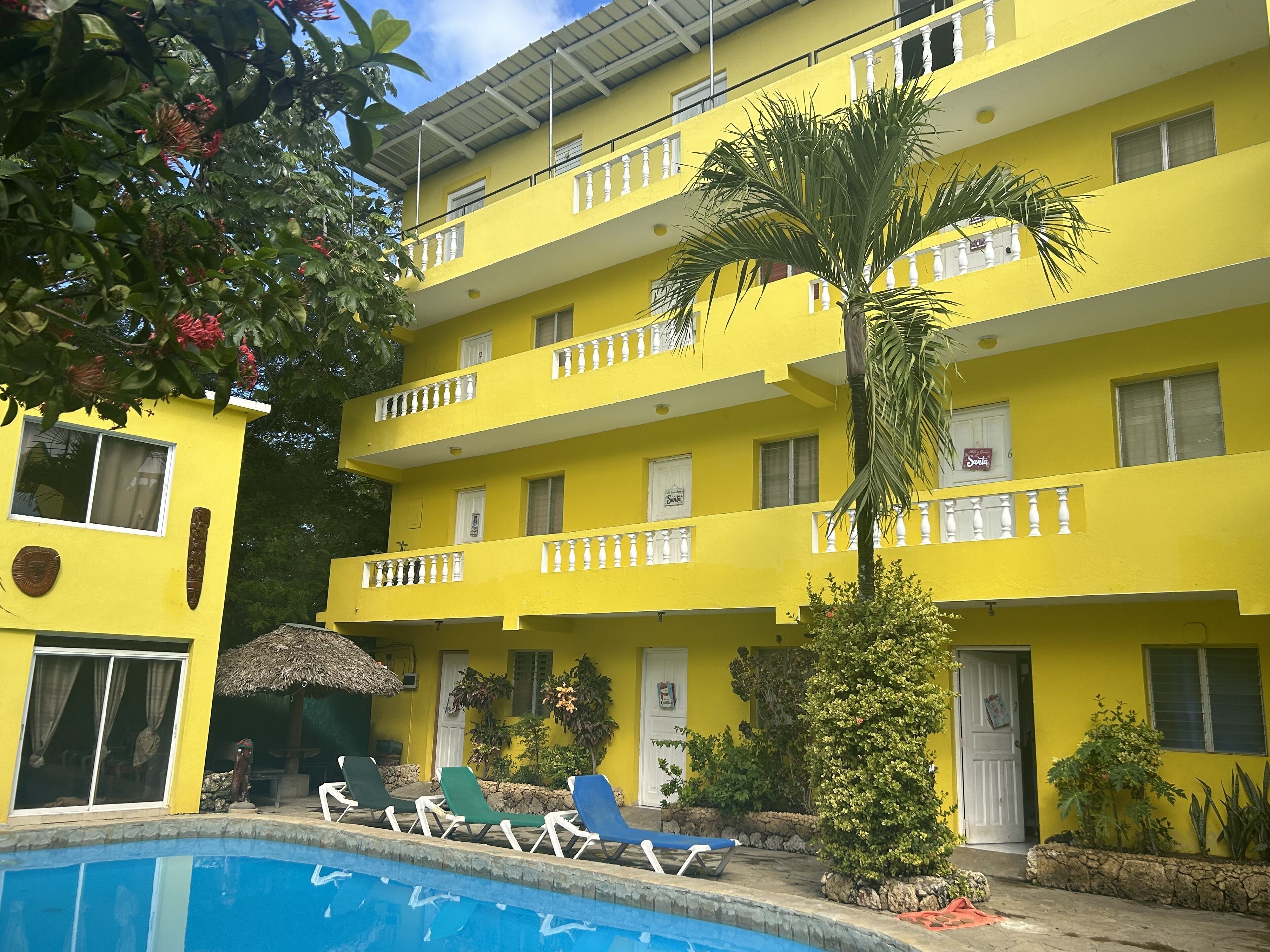 A yellow multi-story building with balconies, a swimming pool, and lounge chairs.
