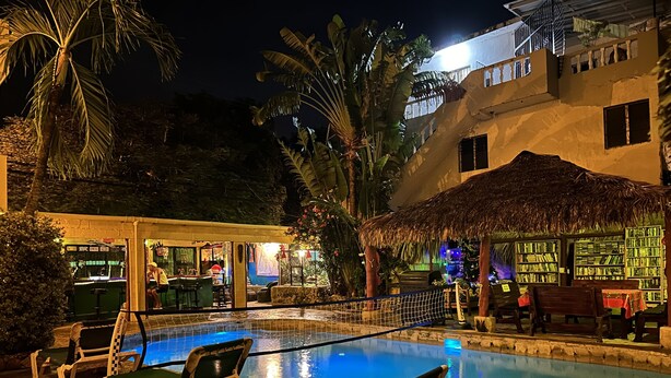 Un espace piscine doté de chaises longues, d’un bar et d’une structure recouverte d’un toit de chaume.