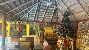 Un intérieur au toit de chaume, avec un sapin de Noël, des sièges et une bibliothèque.