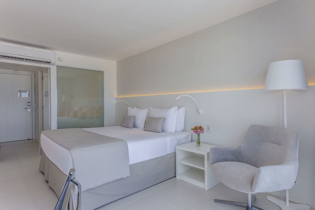 Una habitación de hotel moderna con cama, mesita de noche, silla y un separador de vidrio.