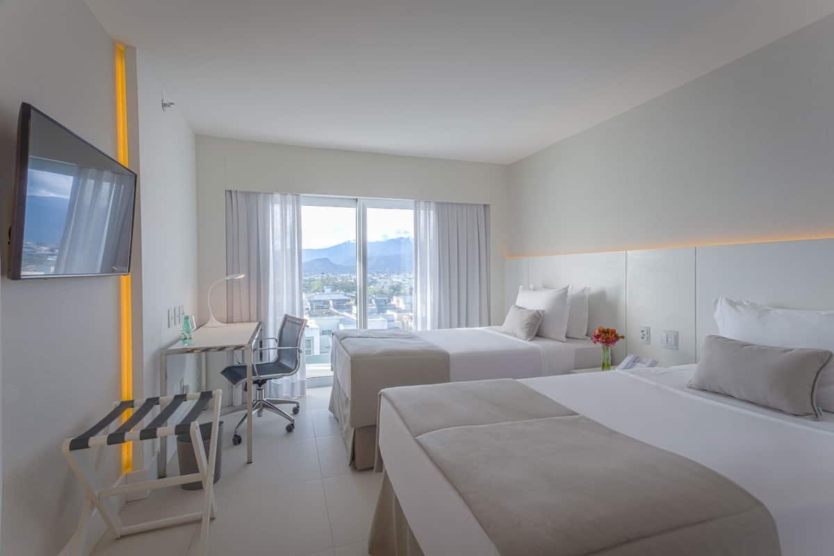 Habitación de hotel con dos camas, un escritorio, una silla, televisión y vistas a la ciudad.