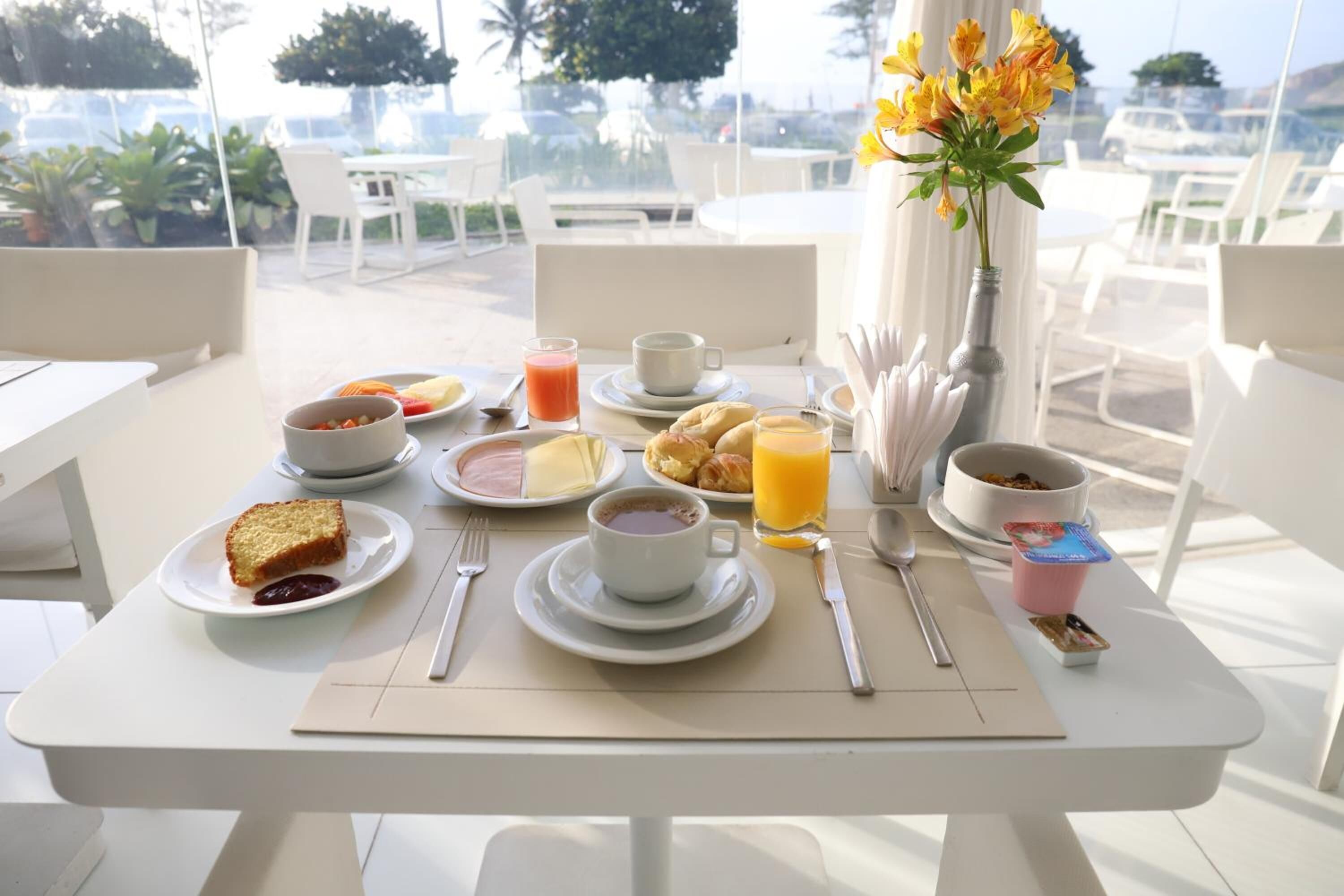 A breakfast table with plates of food, cups, and a vase of flowers.
