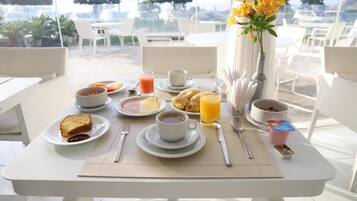 A breakfast table with plates of food, cups, and a vase of flowers.