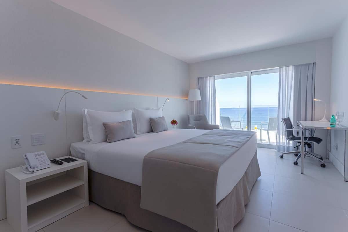 Habitación de hotel moderna con una cama grande, un escritorio, una silla y vistas al océano.
