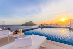 A poolside area with lounge chairs, a table with fruit and drinks, and a view of the ocean and sunset. - CDesign Hotel (Rio de Janeiro)