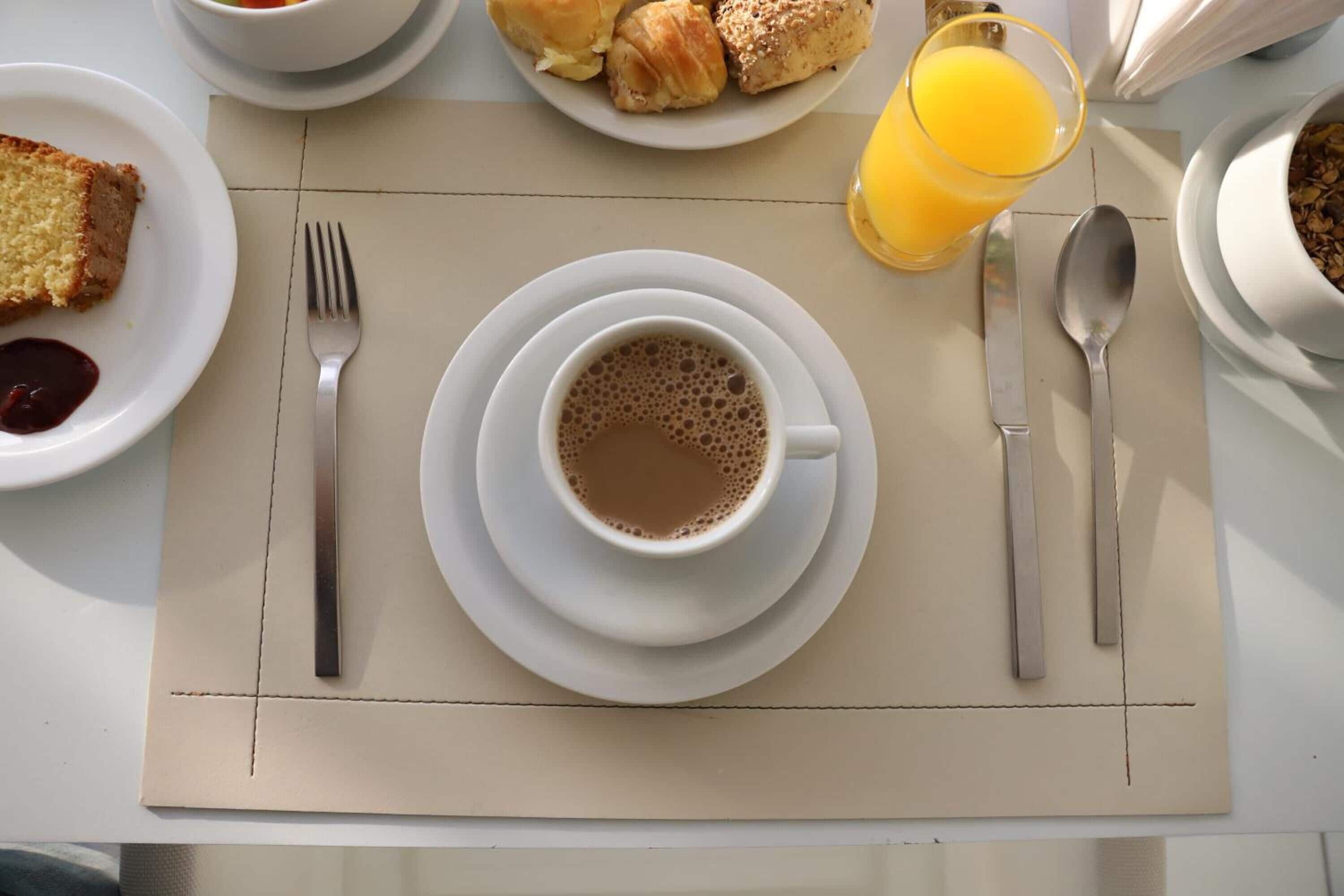 En morgenmadsopsætning med en kop kaffe, croissanter og et glas appelsinjuice på et bord.