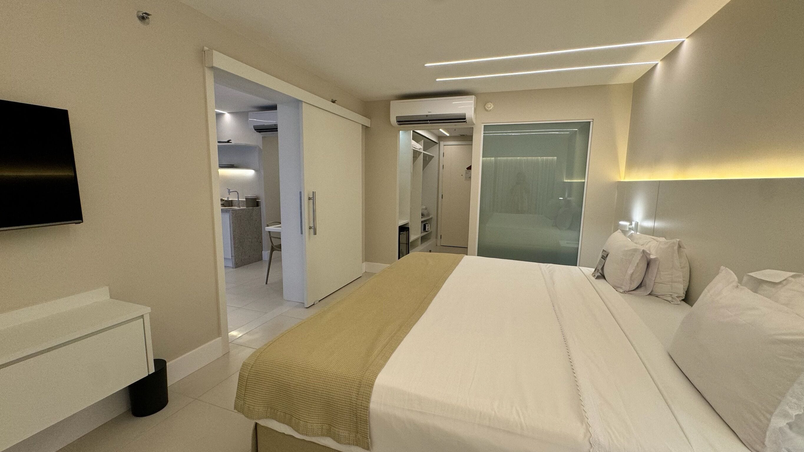 Quarto de hotel com cama, mesa de cabeceira, televisão e um closet espaçoso.