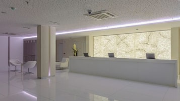 Una zona de recepción moderna con un muro de mármol, un mostrador de recepción y dos sillas blancas.