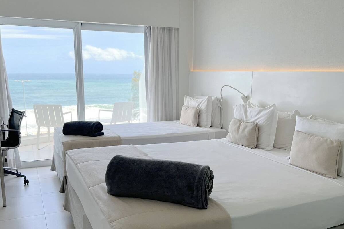 Habitación de hotel con dos camas, un escritorio y vista al océano.
