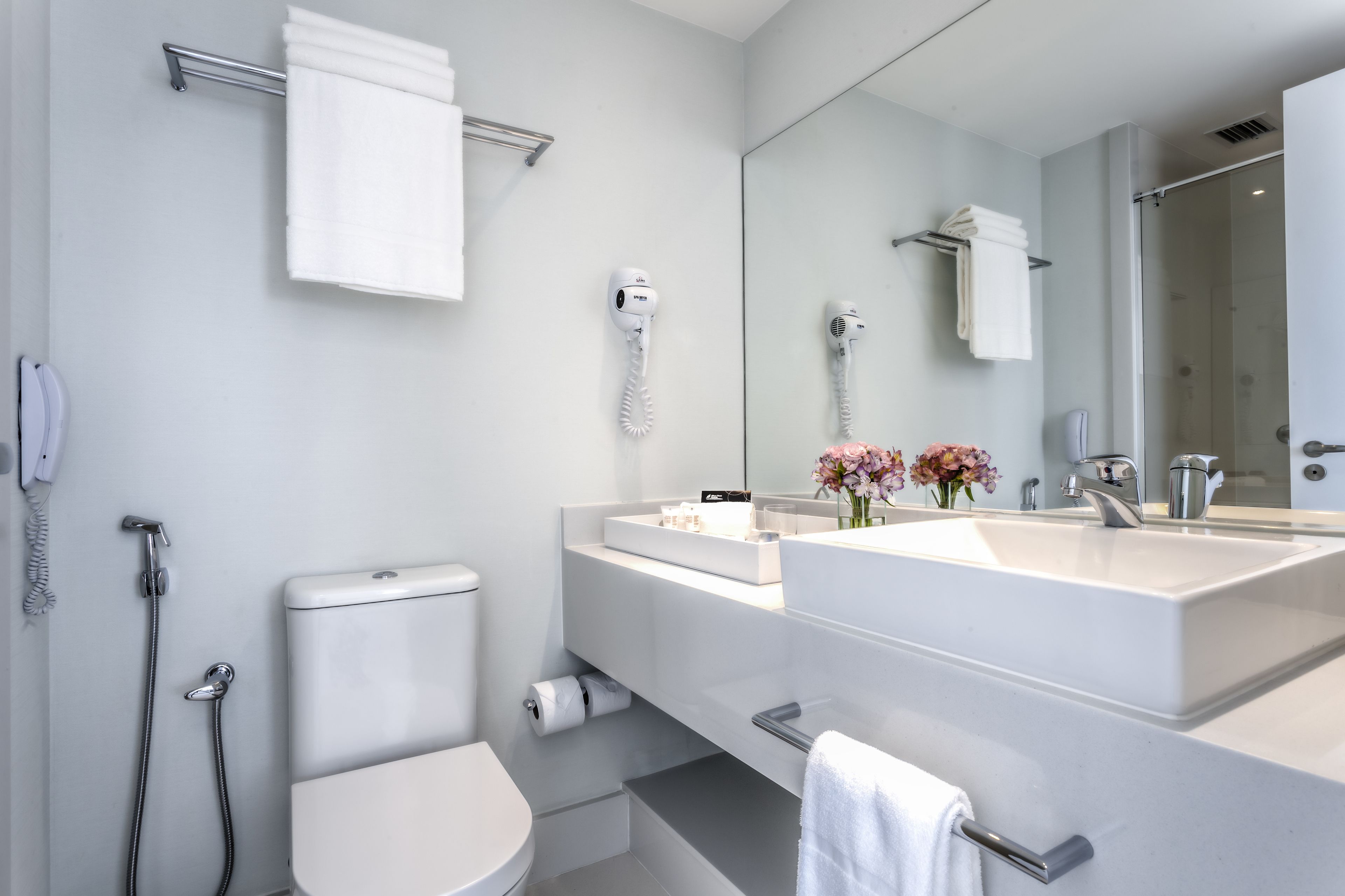 Une salle de bain moderne avec un lavabo blanc, un grand miroir, des toilettes et une douche.