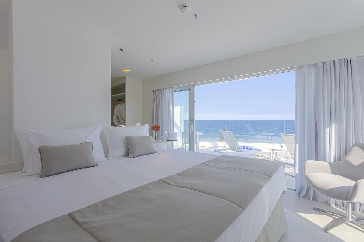 Habitación de hotel con una cama grande, una silla y un balcón con vista al océano.