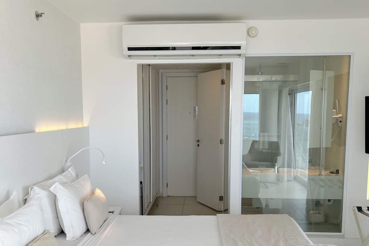 Habitación de hotel con una cama grande, una puerta de vidrio que da al baño y un televisor montado.