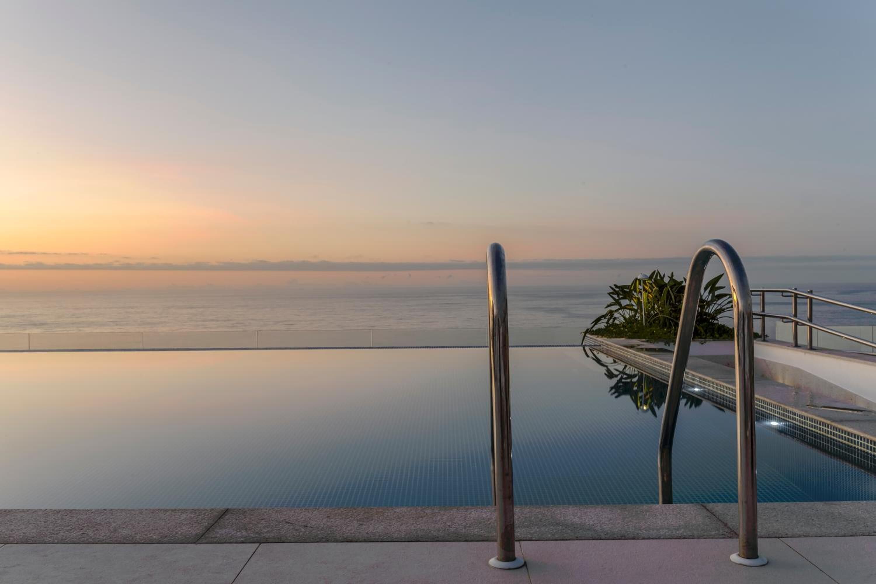 Una piscina infinita con vista al océano al atardecer.