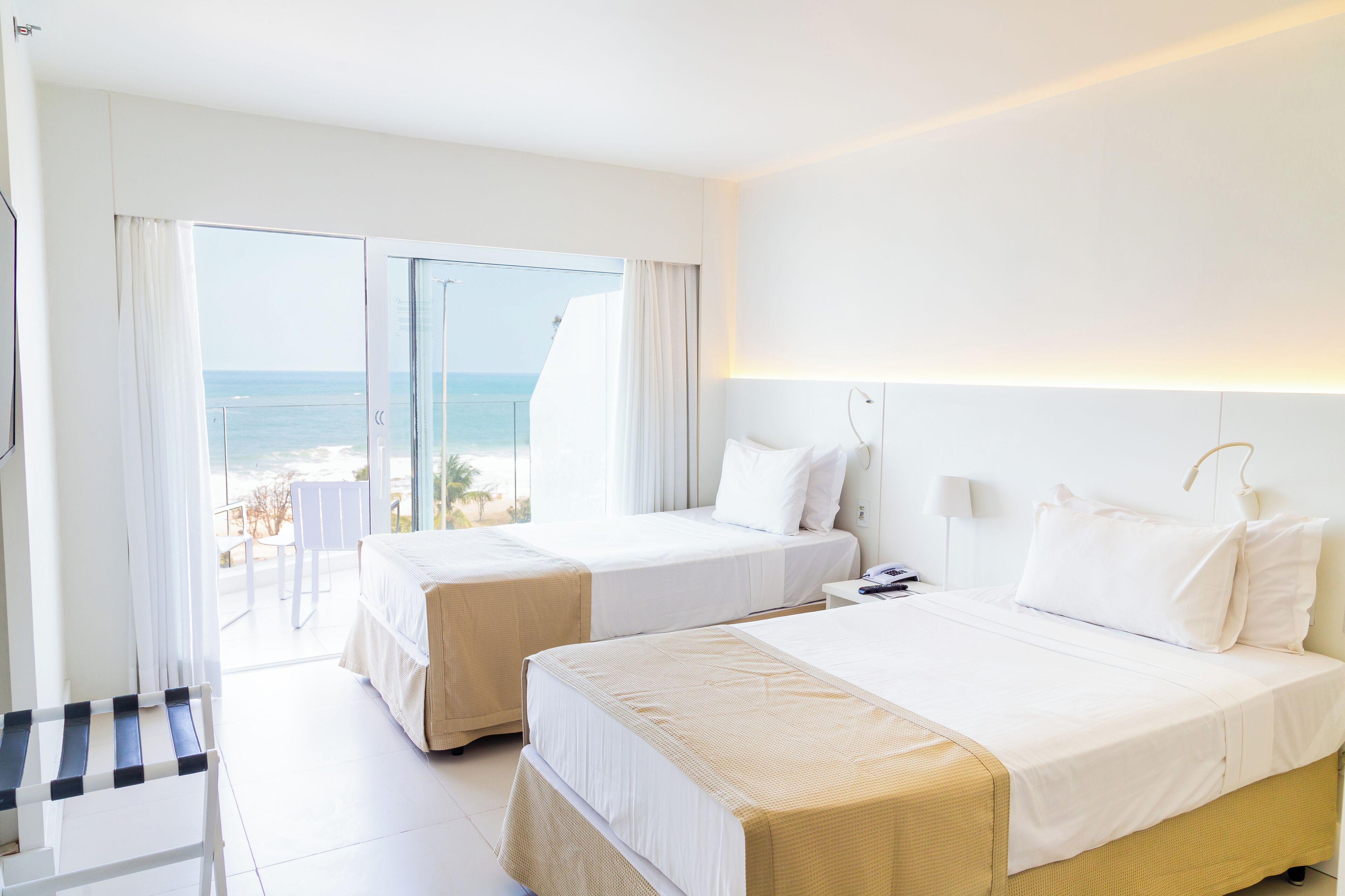 A hotel room with two beds, a balcony with a view of the sea, and a small table.