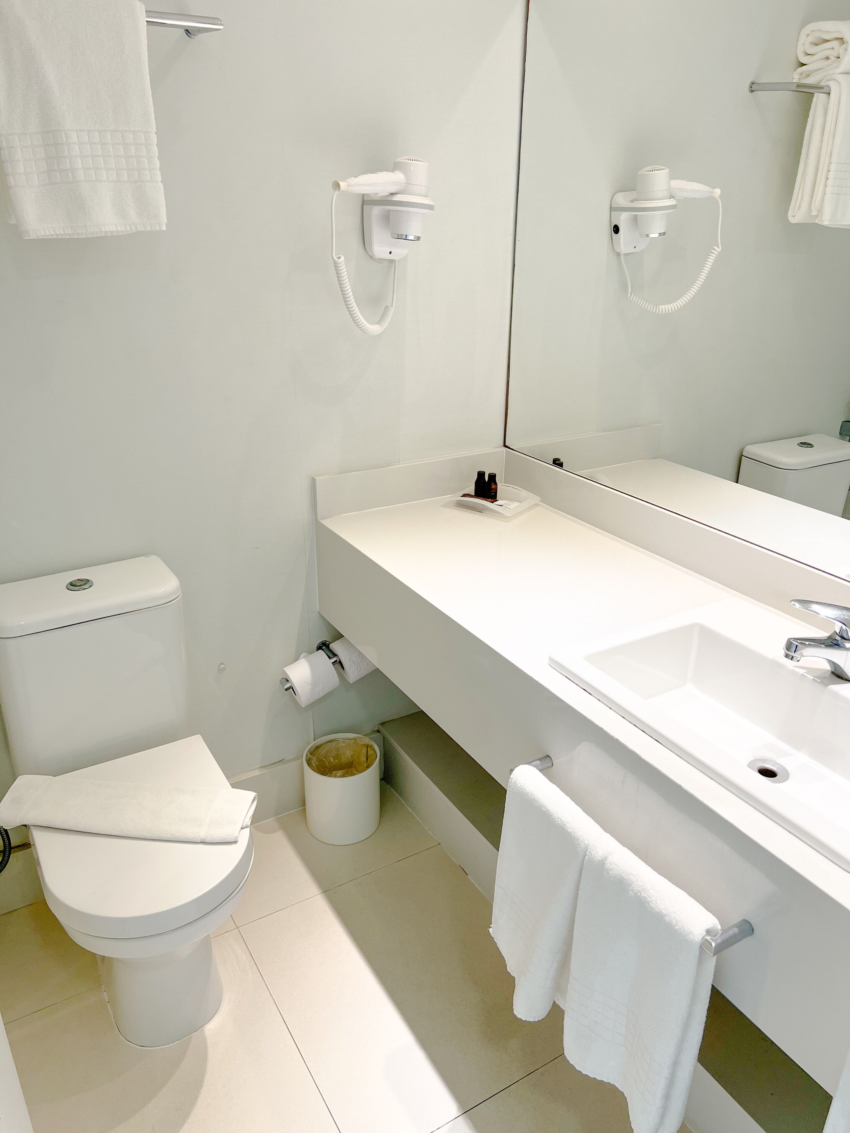 Un baño moderno con un lavamanos blanco, un espejo, un inodoro y un perchero para toallas.