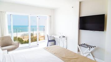 Habitación de hotel con cama, escritorio, silla, televisor y vista al océano.