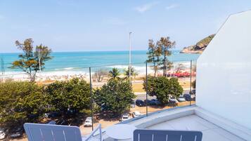Un balcón con vista a una playa, coches estacionados y árboles.