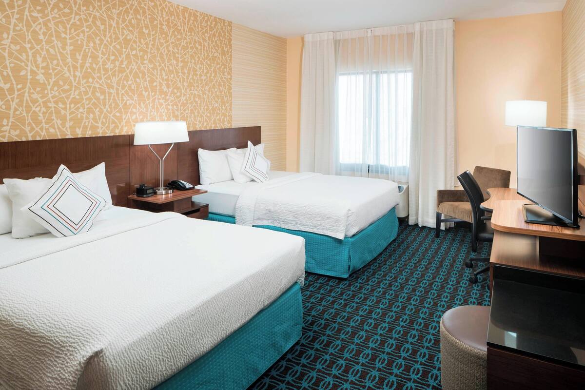 A hotel room with two beds, a desk with a TV, and a window with curtains.