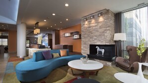 A modern living room with a blue sectional sofa, a fireplace, and a dining area with a bar. - Fairfield Inn & Suites by Marriott Houston Pasadena (Pasadena)