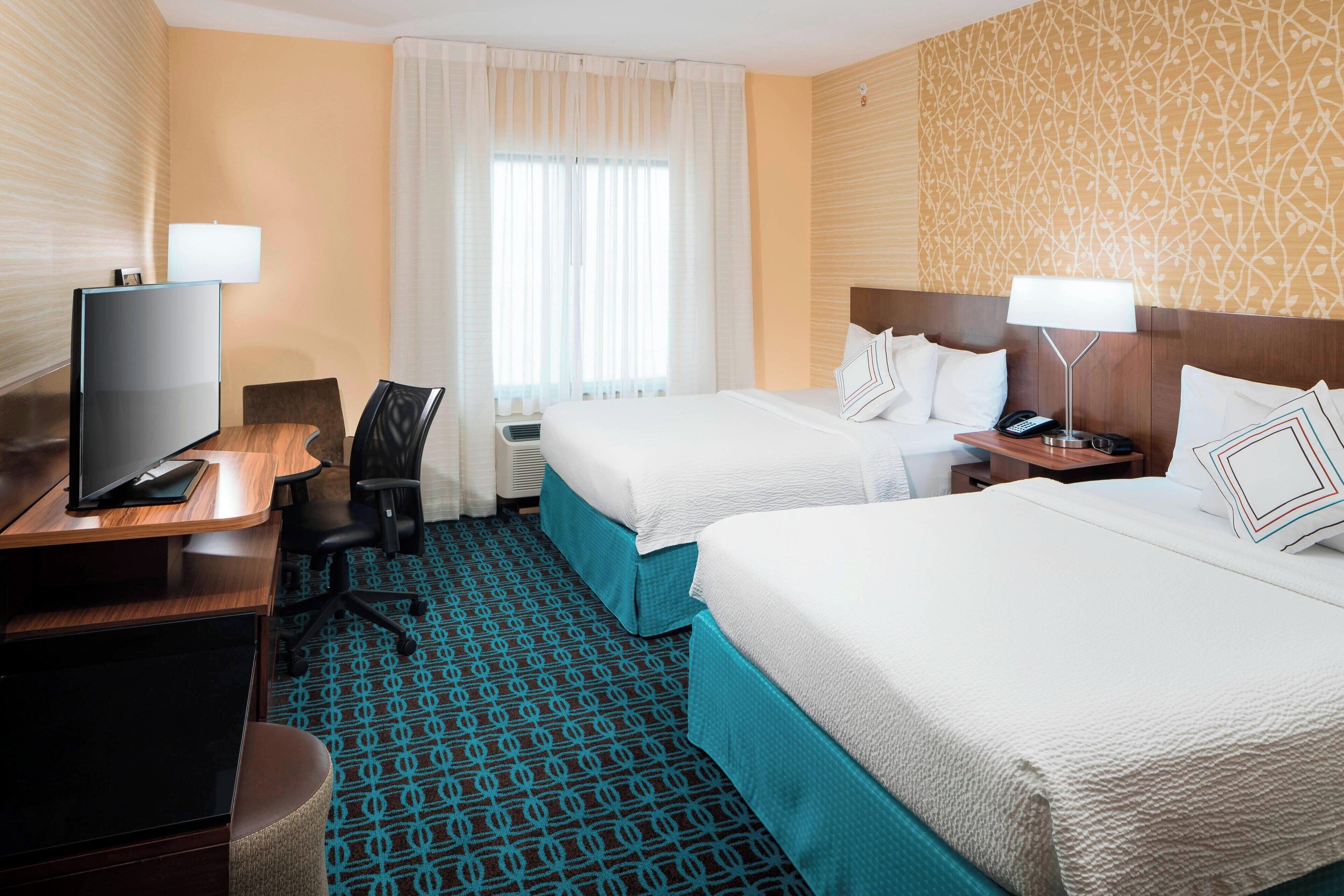 A hotel room with two beds, a desk with a TV, a chair, and a patterned carpet.