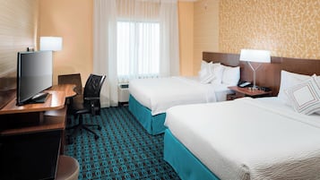 A hotel room with two beds, a desk with a TV, a chair, and a patterned carpet.