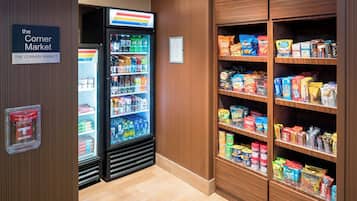 A corner market with a refrigerated drink cooler, shelves stocked with snacks and cereals, and a visible 7-Eleven sign.